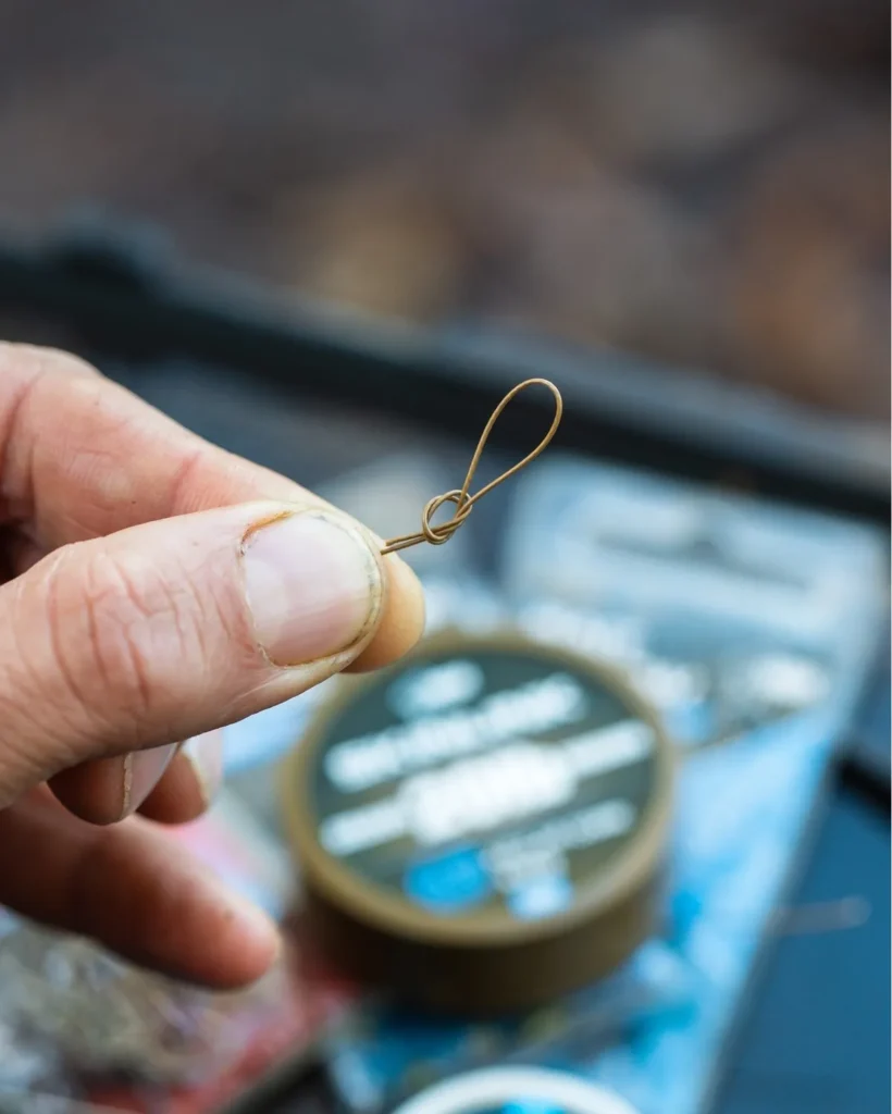 Close-up of a carp rig hooklink join showing two small putty blobs on the coated hooklink, held between fingers on a dark rig surface.