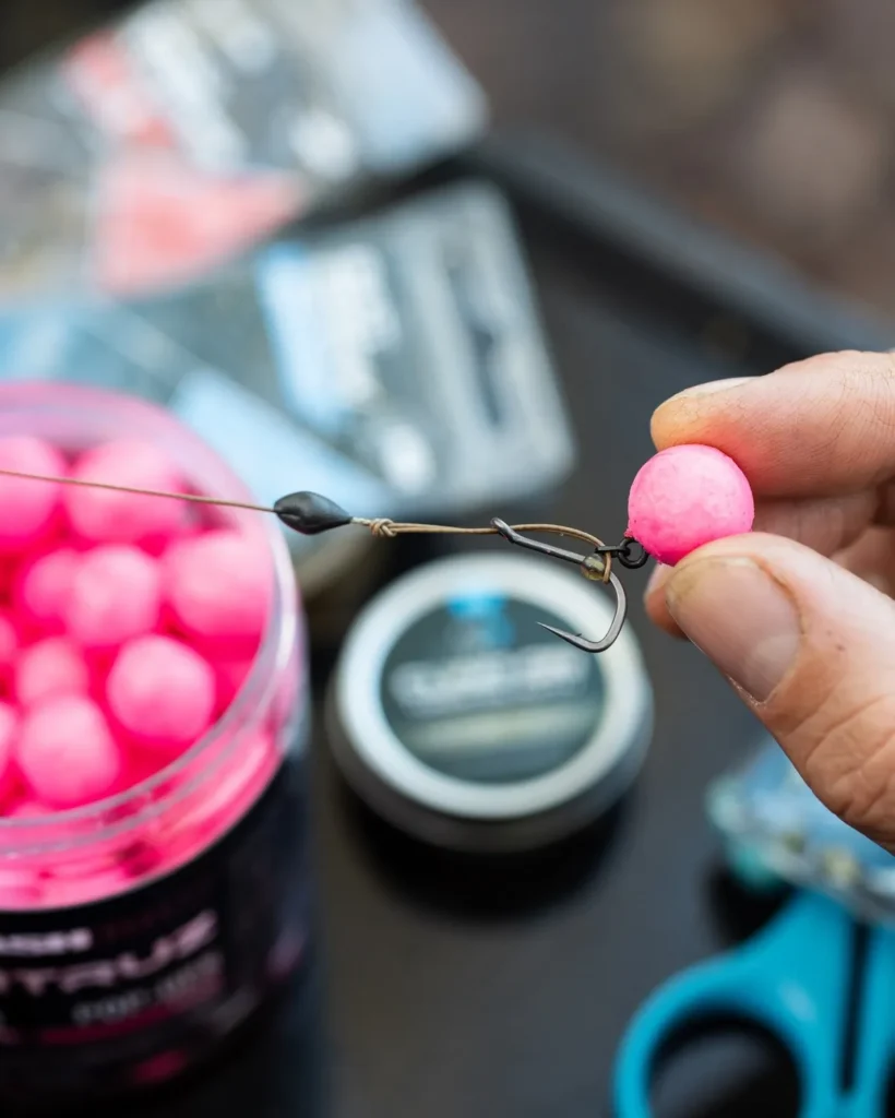 Close-up of a looped coated hooklink tied for a multi rig, held between thumb and forefinger with tackle items blurred in the background.