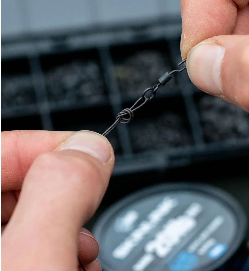 Close-up of hands tying a small Ronnie swivel to a coated hooklink with a neat compact knot.